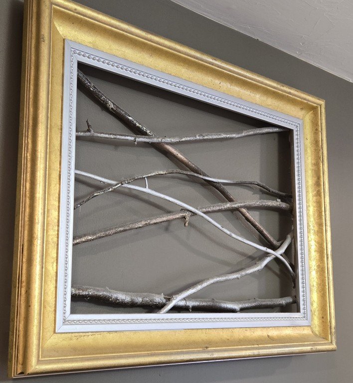 Wall art made with twigs and a picture frame spray painted with metallic spray paint